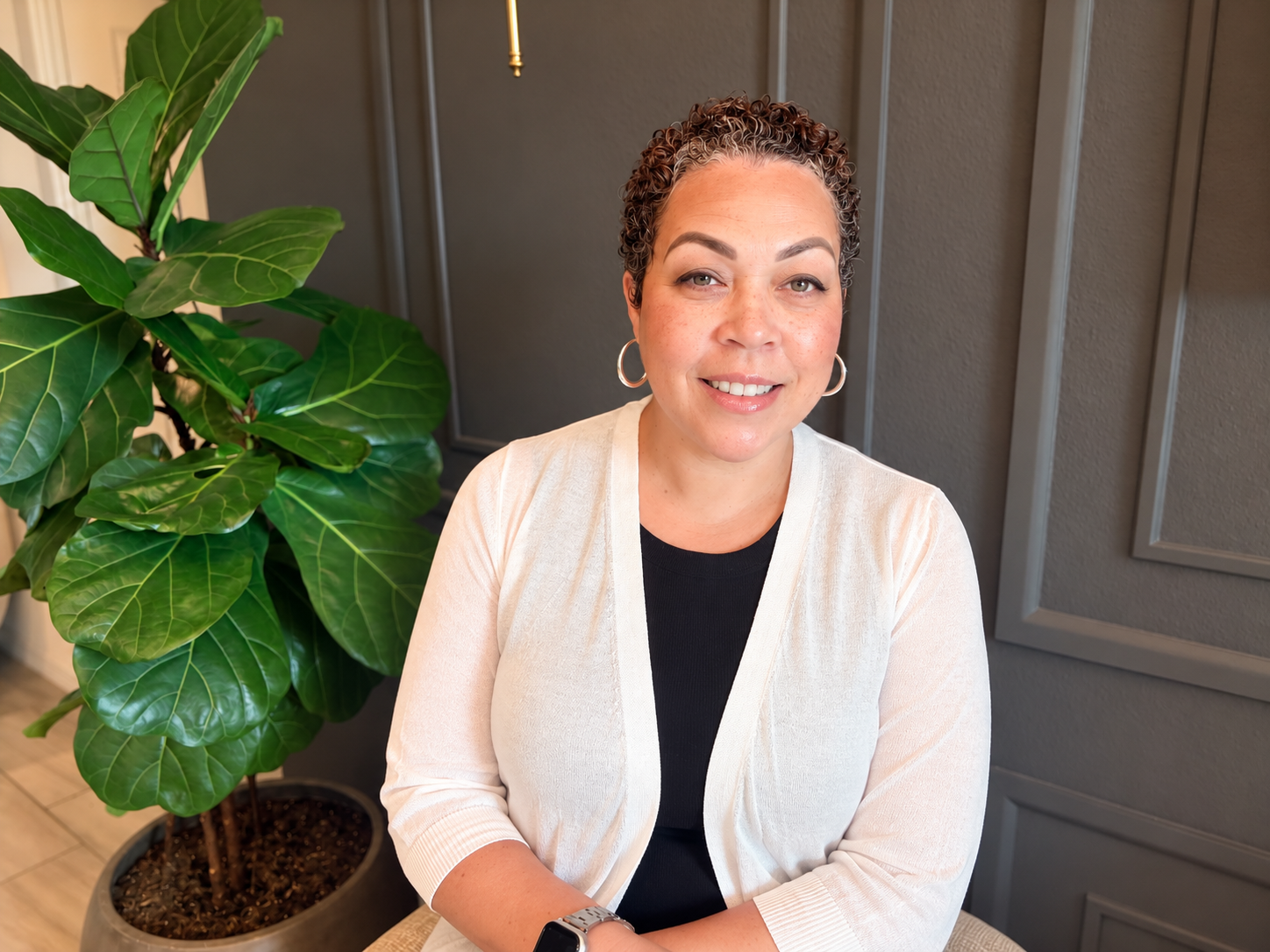 Nicole Wright seated in a warm, modern interior beside a leafy plant